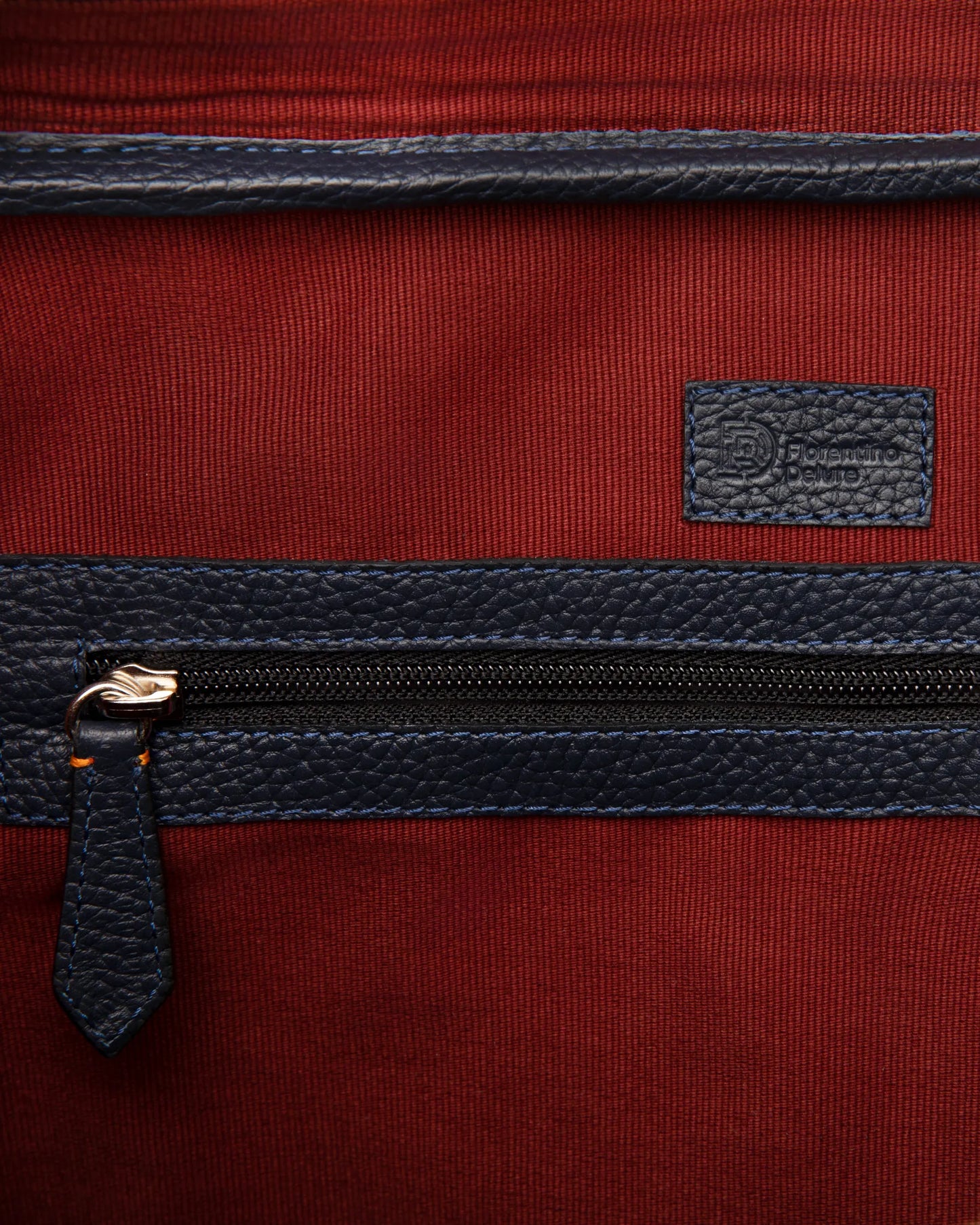 Detaliu geantă Navy Briefcase Florentinodelure, piele albastră, textură metalică, fundal roșu.
