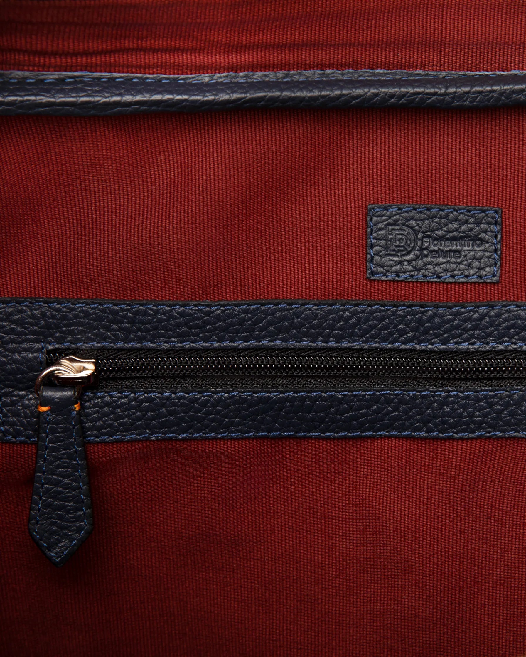 Detaliu geantă Navy Briefcase Florentinodelure, piele albastră, textură metalică, fundal roșu.
